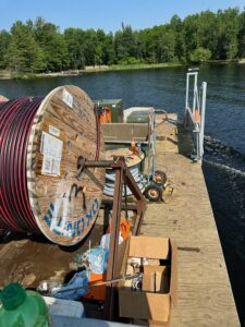 A spool of power line and tools on a dock on a body of water